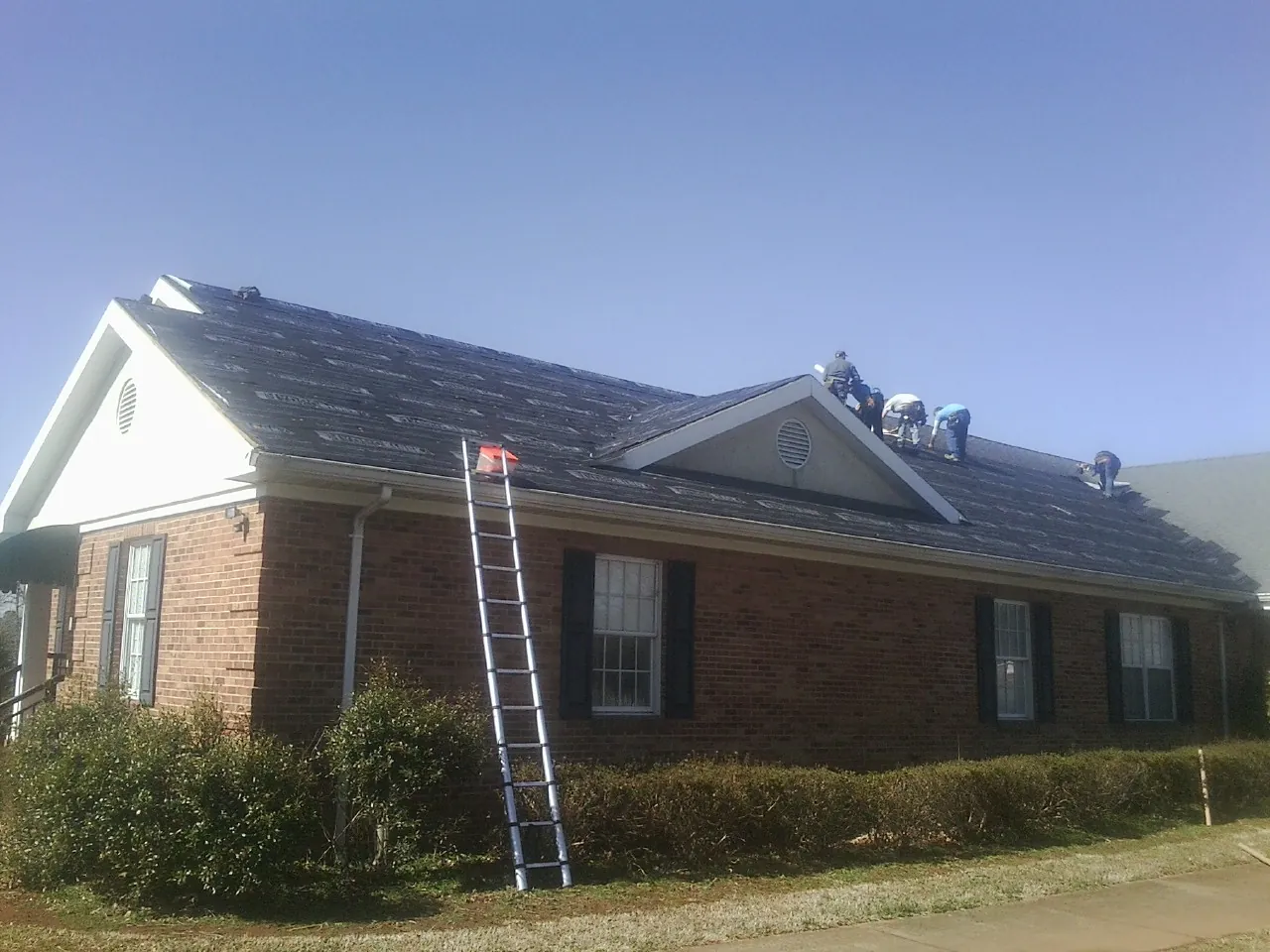 Crew tearing shingles off a brick ranch roof with a ladder set — Metal Roof Repair work by our crew in Susanville