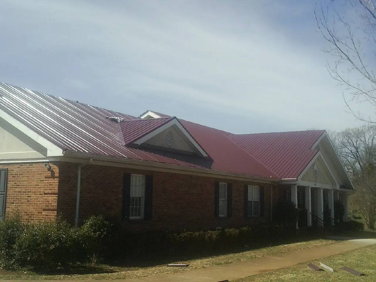 Red metal roof with gabled entries on a long brick building, from a Hail Damage Roof Repair job in Susanville