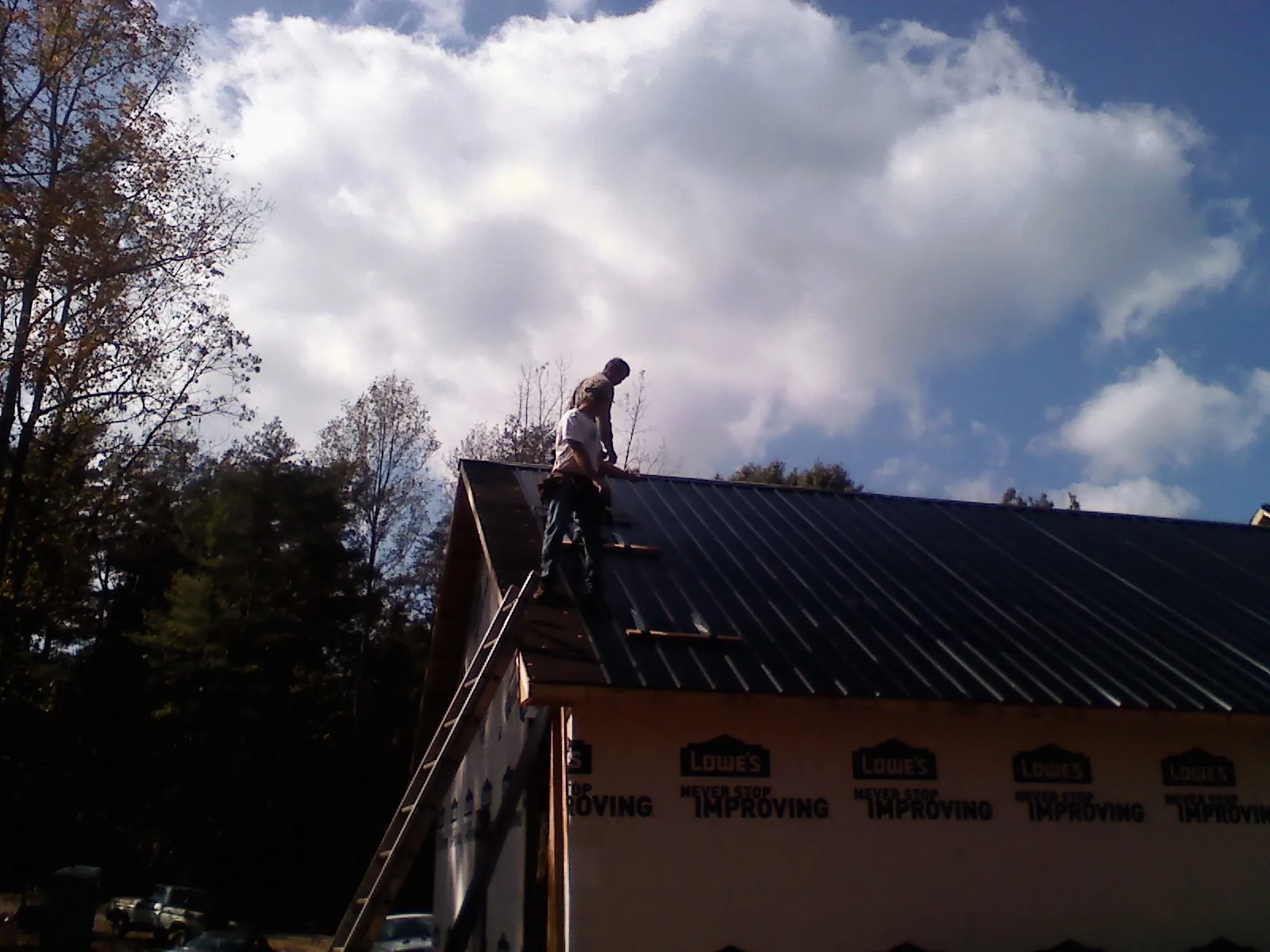 Roofer fastening dark metal panels high against a cloudy sky, from a Roof Inspection job in Susanville