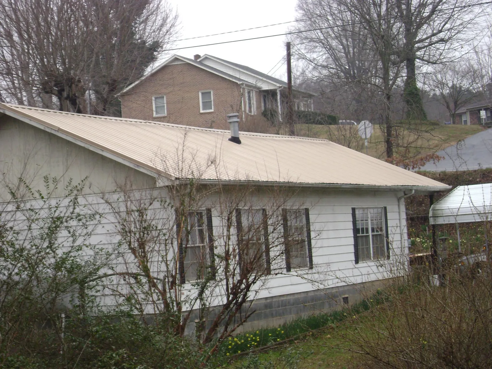 Tan metal roof on a white sided house set into a hillside — Commercial Roofing by Roofing Brothers in Susanville